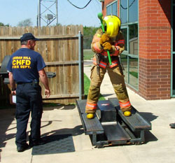 Fire fighter using sledge hammer to move an I-beam, while standing on the sled.